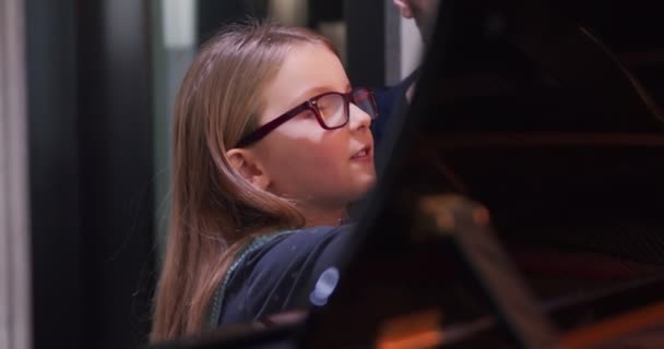 Малюк вчиться грати на піаніно від вчителя. Маленька дівчинка вивчає аркуш музики читання. Назад вид крупним планом. Класи Піано з учителем та навчанням дітей. Класи Піано вдома. Дитина вчиться піаніно від свого батька — стокове відео