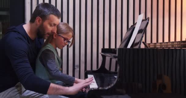 Тато викладає фортепіано своїй дочці. Маленька дівчинка вивчає фортепіано вдома. Дитина вчиться піаніно від свого батька — стокове відео