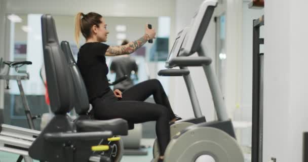 Mulher se exercitando com elíptico cross trainer no ginásio.Vista lateral, câmera lenta. Treino de mulher em bicicleta elíptica. Mulher pedalando no ginásio — Vídeo de Stock