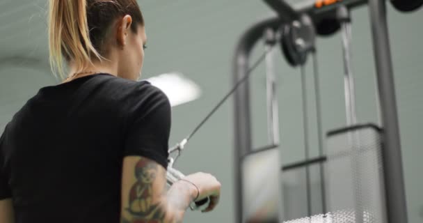 Mujer haciendo ejercicio con la barra de tríceps de cable en el gimnasio.Vista trasera, cámara lenta. Entrenamiento de mujer en la máquina de empuje de tríceps — Vídeo de stock