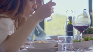 Evde spagetti yiyen bir kadın. Makarna yiyen kadın. Yan görünüş yakın. Bir grup insan birlikte konuşuyor, yemek yiyor, şarap içiyor. Arkadaşlar modern ev yemeği veya öğle yemeği partilerinin tadını çıkarıyorlar.