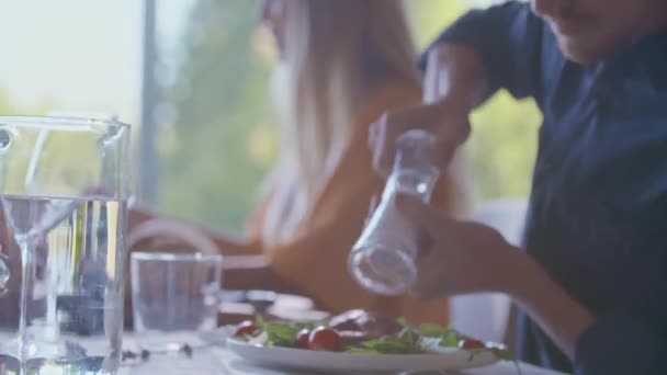 Detail van de mens kruiden gegrild vlees met zout shaker aan eettafel. Handen van dichtbij, handheld. Man zout gegrild vlees detail. Mankruidensalade. — Stockvideo