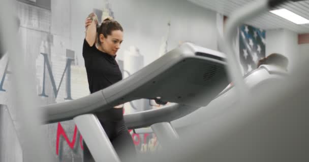 Młoda kobieta rozciągająca się na bieżni na siłowni. Pani trenuje w centrum fitness. Kobieta ćwiczy cardio workout — Wideo stockowe