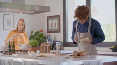 Kadın modern mutfakta yemek pişiriyor ve kontrol ediyor. Erkek peyniri kavrıyor. Gençler öğle veya akşam yemeği için evde yemek pişiriyor. Modern açık alan mutfağı