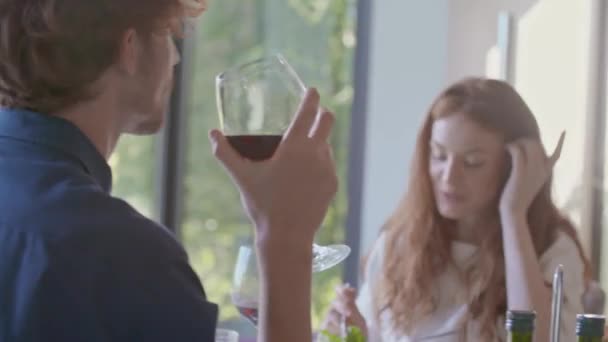 Hombre hablando con amigos durante el almuerzo en casa mientras guarda una copa de vino. Personas hablando y comiendo en la mesa de comedor — Vídeo de stock