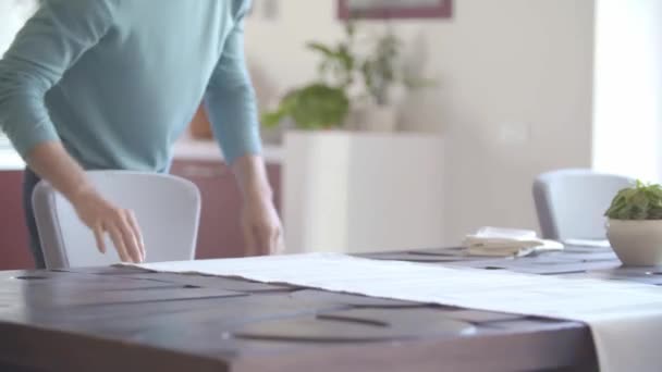 Dos personas colocando la mesa en la sala de estar poniendo platos para la comida mientras hablan entre sí.Gente feliz grupo disfrutar de la cena o almuerzo casera moderna. — Vídeos de Stock