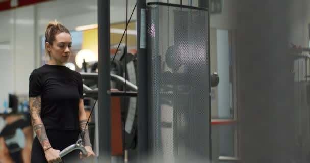 Mujer haciendo ejercicio con la barra de tríceps de cable en el gimnasio.Vista trasera, cámara lenta. Entrenamiento de mujer en la máquina de empuje de tríceps — Vídeo de stock