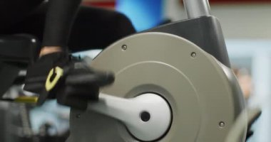 Kadın spor salonunda eliptik çapraz antrenörle egzersiz yapıyor. Yan görüş, pedal çevirme, ağır çekim. Eliptik bisiklette kadın eğitimi. Spor salonunda pedal çeviren kadın.