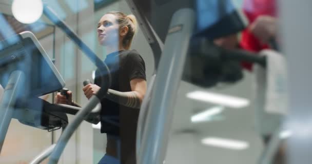 体操で楕円歩行機で運動する女。フロントビュースローモーション。ウォーキングマシンで女の訓練。ジムのマシンを歩く女性 — ストック動画