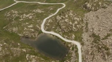 Sinematik hava manzaralı çakıl yolu dağdaki küçük göl yakınında. Bulutlu, sisli ve puslu. İlerle.