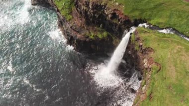 Uçurum manzarasından çarpıcı bir şelale fışkırıyor. Faroe Adaları 'ndaki Gasadalur Köyü yakınlarında Mulafossur şelalesi. Havadan çekim, gün ışığı, bulutlu hava