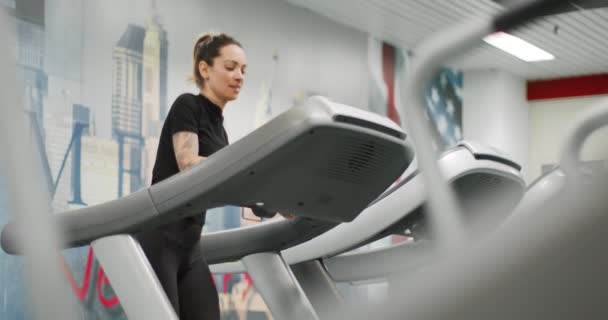 Wanita muda memilih latihan rutin pada treadmill di gym. Pemandangan depan. Pelatihan wanita di pusat kebugaran. Perempuan yang berolahraga kardio — Stok Video