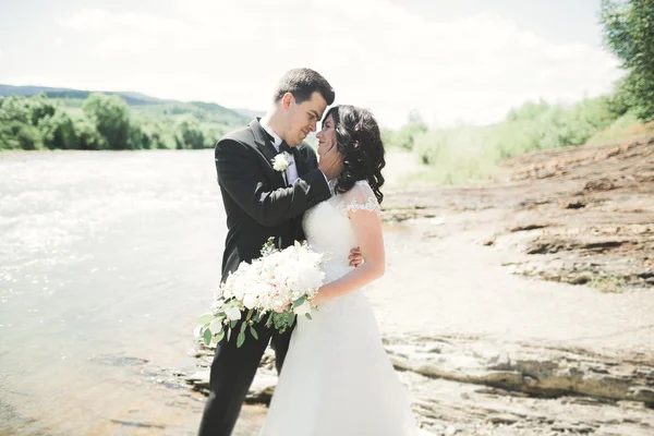 Elegante novio elegante y elegante novia cerca del río con piedras. Pareja de boda enamorada —  Fotos de Stock