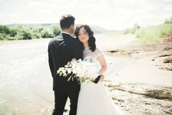 Nevěsta a ženich drží krásné svatební kytice. Pózování v blízkosti řeky — Stock fotografie