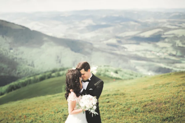 Giovane coppia appena sposata, sposa e sposo baciare, abbracciando sulla vista perfetta delle montagne, cielo blu — Foto Stock