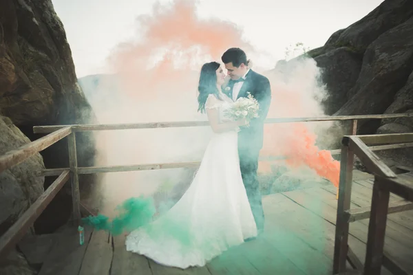 그들 뒤에 착 색 된 연기와 함께 바위 근처 커플 포즈 웨딩 — 스톡 사진
