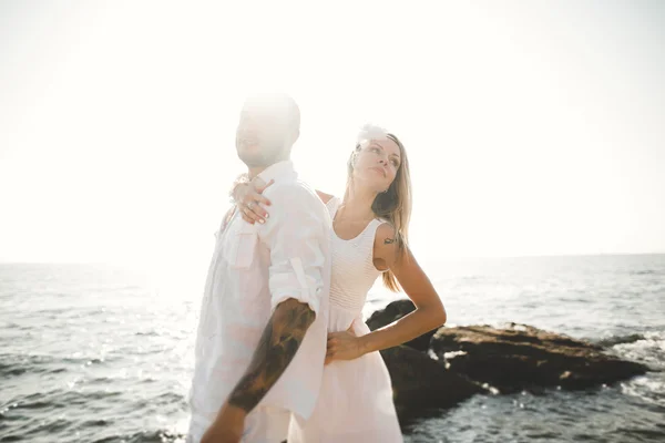 Romántica pareja amorosa posando sobre piedras cerca del mar, cielo azul — Foto de Stock