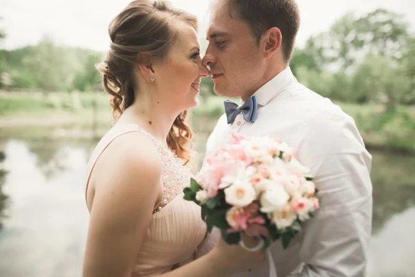 Bride and groom holding beautiful wedding bouquet. Lake, forest — Stock Photo, Image