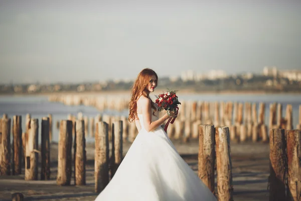 Romantica bella sposa in abito bianco in posa sullo sfondo mare e pali di legno — Foto Stock