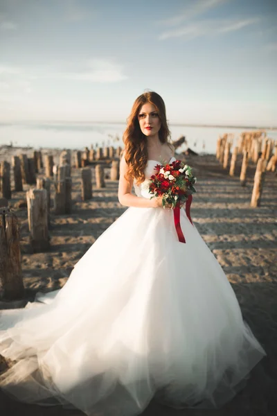 Romantica bella sposa in abito bianco in posa sullo sfondo mare e pali di legno — Foto Stock