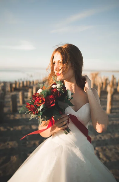 Красивая молодая невеста с свадебным букетом позирует на фоне моря — стоковое фото