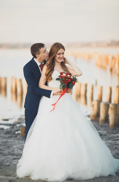 Beau jeune couple de mariage, mariée et marié posant près des poteaux en bois sur la mer de fond — Photo