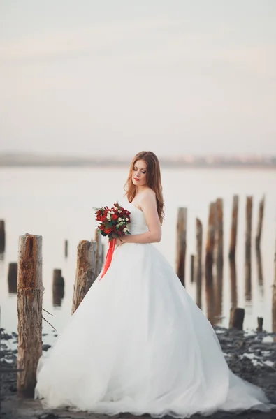 Romantica bella sposa in abito bianco in posa sullo sfondo mare e pali di legno — Foto Stock