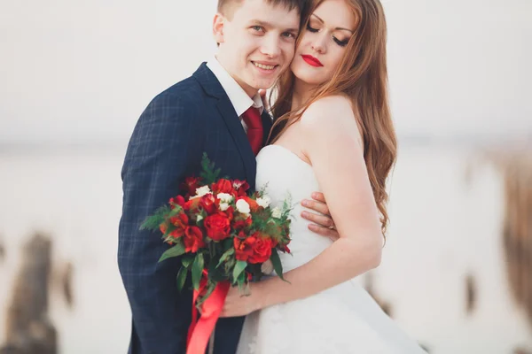 Красива молода весільна пара, наречена і наречений позує біля дерев'яних полюсів на фоні моря — стокове фото
