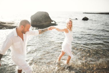 Düğün çifti mavi denizin yanındaki kayalarda öpüşüyor ve sarılıyor.