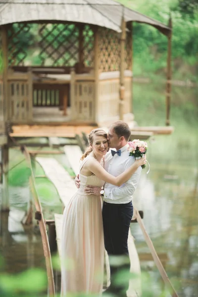 Lovely couple in love kissing each other on the day wedding, standing in the park outdoors near lake — Stock Photo, Image