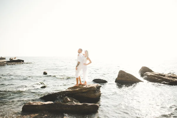 Boda pareja besándose y abrazándose en rocas cerca de mar azul — Foto de Stock