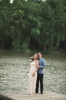 Zarif güzel düğün çifti bir göl kenarında günbatımında poz
