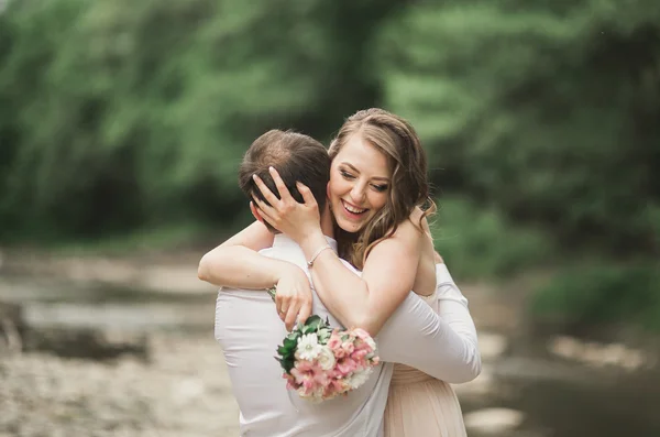 Elegante noivo elegante doce e noiva perto do rio com pedras. Casamento casal apaixonado — Fotografia de Stock