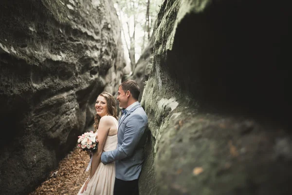 Hermosa pareja de boda besándose y abrazándose en el bosque con grandes rocas — Foto de Stock