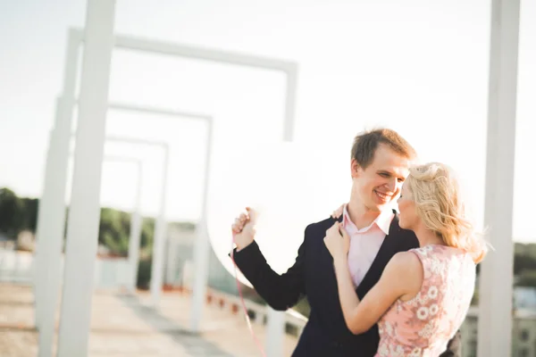 Jeune couple amoureux posant sur le toit avec vue parfaite sur la ville tenant la main et étreignant. Beau coucher de soleil — Photo