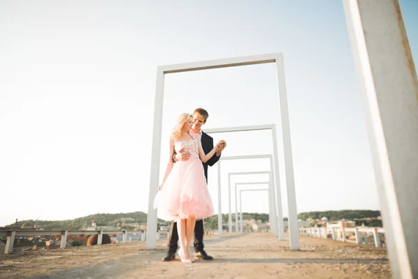 Pareja joven enamorada posando en el techo con una vista perfecta de la ciudad cogida de la mano y abrazándose. Hermoso atardecer — Foto de Stock