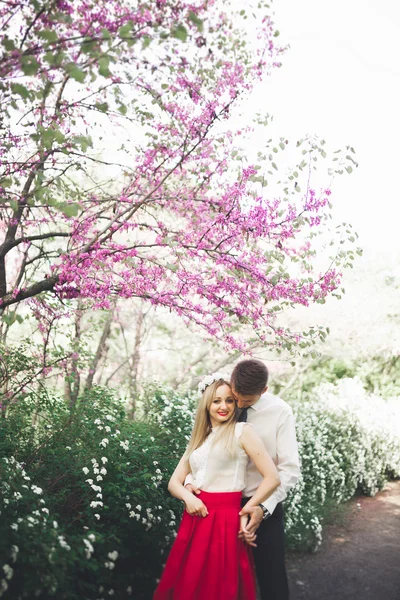 Joven hermosa pareja besándose y abrazándose cerca de los árboles con flor en el parque de verano —  Fotos de Stock