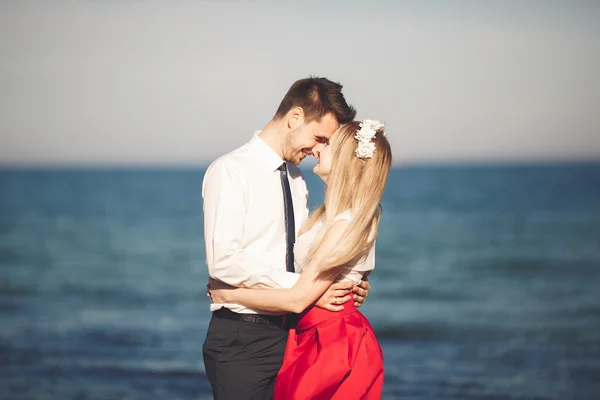 Junges glückliches Paar, das lächelnd am Strand spaziert und sich umschlingt. Liebesgeschichte — Stockfoto