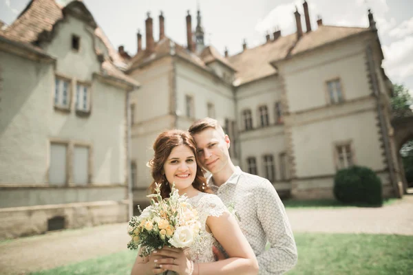 Щаслива весільна пара обіймає і посміхається один одному на фоні старого замку — стокове фото