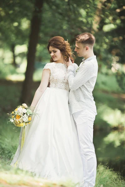 Casal elegante de recém-casados felizes andando no parque em seu dia de casamento com buquê — Fotografia de Stock