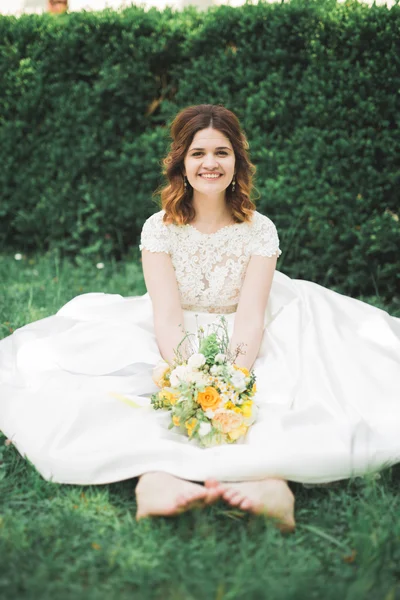 Preciosa novia sentada en el suelo sosteniendo un ramo sonriendo a la cámara — Foto de Stock