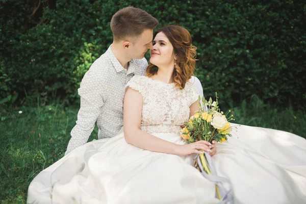 Elegante coppia di sposi felici che passeggiano nel parco il giorno del loro matrimonio con bouquet — Foto Stock