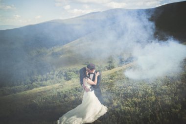 Güzel bir düğün çifti mükemmel bir manzarayla dağda öpüşüyor ve sarılıyor.