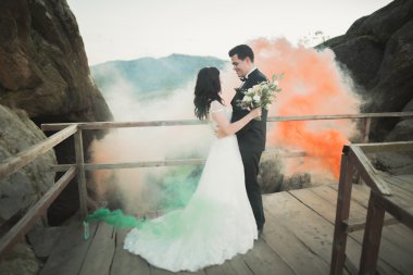 Çift yakınındaki kayaların arkasında renkli duman ile poz düğün