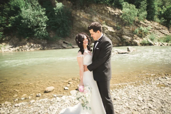 Элегантный нежный стильный жених и невеста возле реки с камнями. Свадебная пара влюблена — стоковое фото
