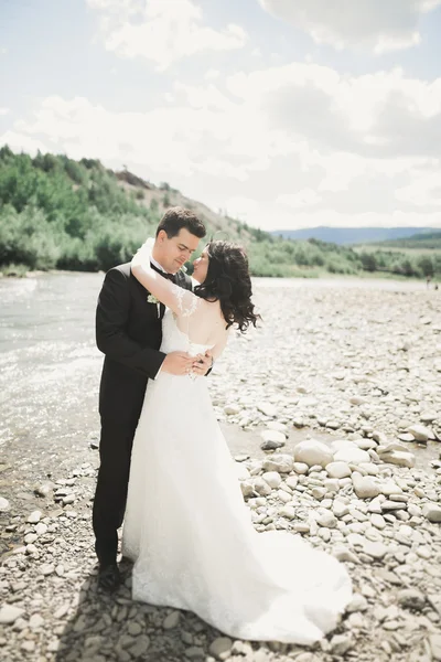 Bellissimo matrimonio coppia baciare e abbracciare vicino alla riva di un fiume di montagna con pietre — Foto Stock