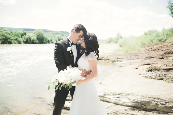 Panna młoda i pan młody, trzymając bukiet piękny ślub. Pozowanie w pobliżu rzeki — Zdjęcie stockowe
