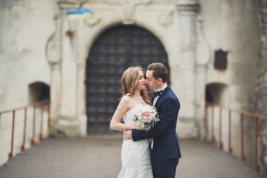 Güzel, romantik bir düğün. Yeni evliler. Eski kalenin yakınlarında sarılıyorlar.