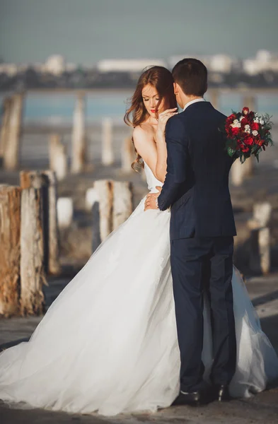 Pareja de boda, novio, novia con ramo posando cerca del mar al atardecer — Foto de Stock