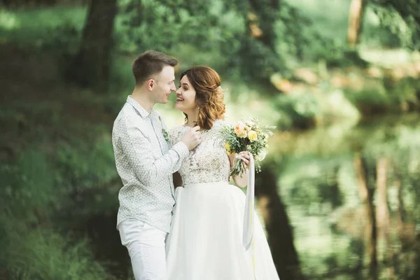 Elegante pareja de recién casados felices caminando en el parque el día de su boda con ramo —  Fotos de Stock